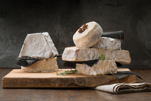 table with a variety of cheeses, stacked on a wooden board.