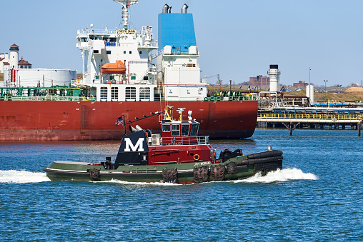 Bayonne, NJ USA - April 6, 2021: Tanker Pacific Sarah is docked at the IMTT Bayonne Bulk Liquid Terminal. The JRT Moran Tug moves eastward on the Kill Van Kull, a tidal strait between Staten Island, NY and Bayonne, NJ.