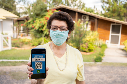 Senior woman with Vaccine passport and face mask.