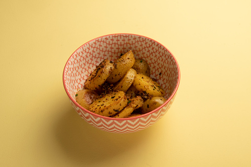 bowl of sliced potato salad seasoned with spices in a yellow table