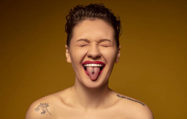 The young woman with a piercing on her tongue closed her eyes and stuck her tongue out. The young woman with a piercing on her tongue closed her eyes and stuck her tongue out. piercing stock pictures, royalty-free photos & images