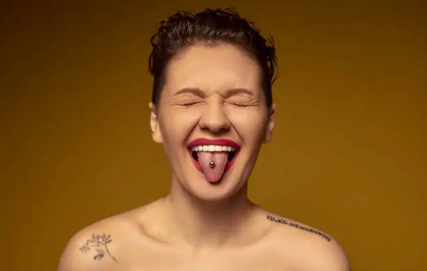 Photo of The young woman with a piercing on her tongue closed her eyes and stuck her tongue out.