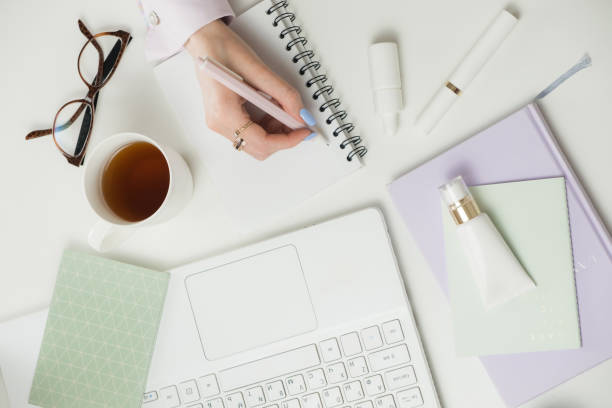 istock Female hands writes in notebook on Office white desktop. Planning Remote working from home. Freelancers laptop, cup, spectacles. Concept of distance learning, isolation, female business 1317351897