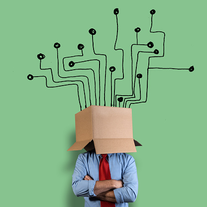 Businessman hiding his head in a cardboard box. He is in front of a circuit board hand drawn on a green wall