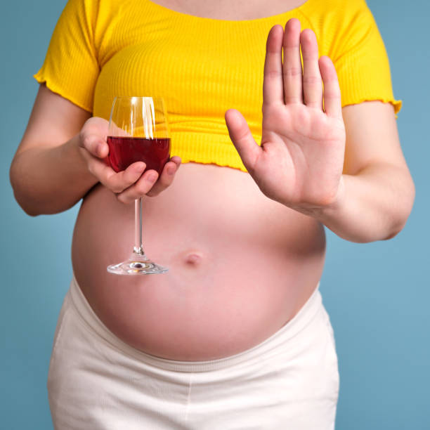 alcol nelle mani di una donna incinta su sfondo blu - abdomen addiction adult alcohol foto e immagini stock