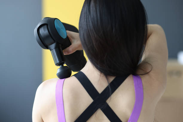 Woman doing massage of muscles of neck and back with percussion massager closeup Woman doing massage of muscles of neck and back with percussion massager closeup. Recovery after sports training concept percussion instrument stock pictures, royalty-free photos & images