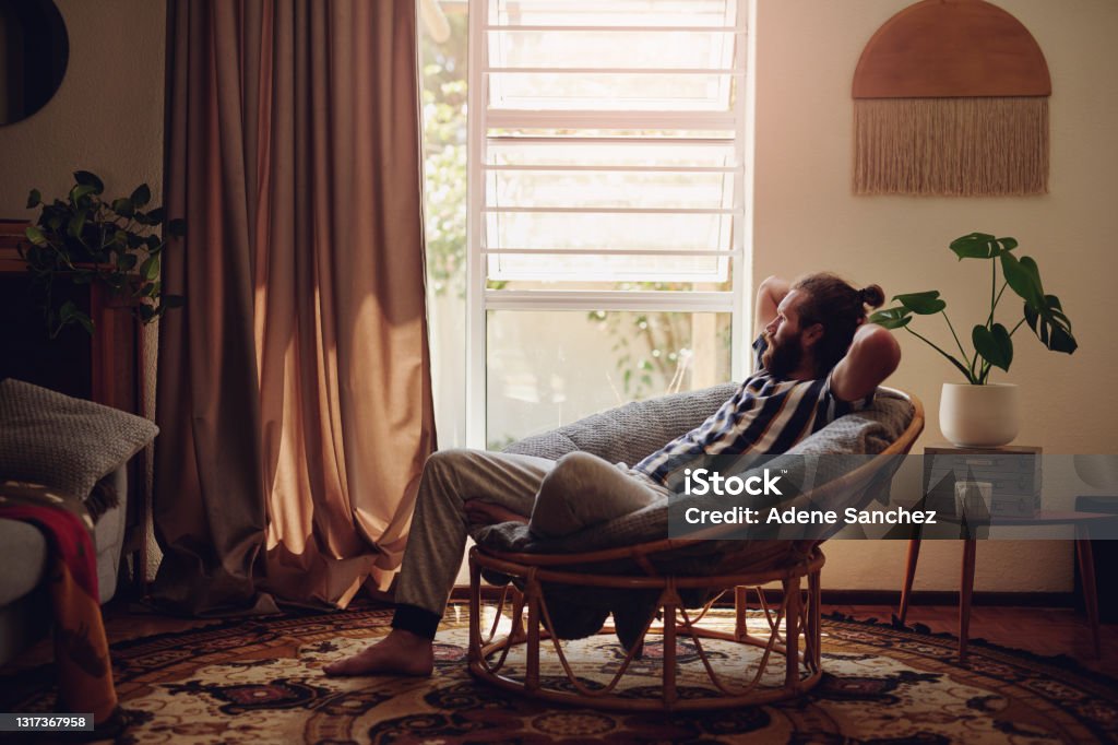 Shot of a young man relaxing on a chair at home I could chill here all day Relaxation Stock Photo