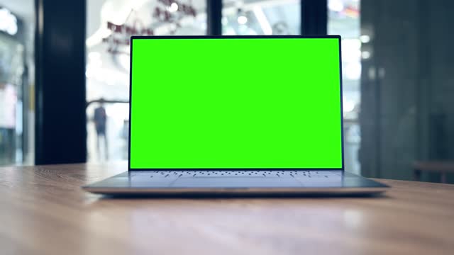 Laptop computer with blank green screen on the table in cafe