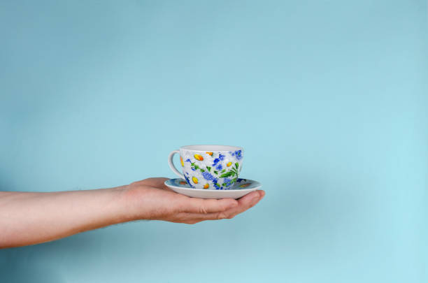 Hand and cup on blue background. Man holding White cup with painted flowers.