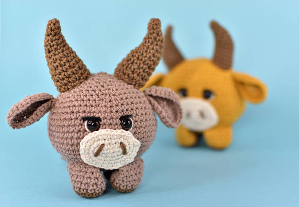 istock Two bulls knitted from thick cotton yarn. They are placed on a blue background and standing one after another. 1317381408