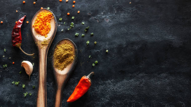 spices in wooden spoons and dry red peppers on a black background with place for text