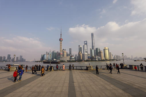 Shanghai, China - 12 01 2017: Commuters and tourist are walking on The Bund waterfront promenade. The Bund is a waterfront area view to Shanghai China modern skyscrapers skyline urban city.