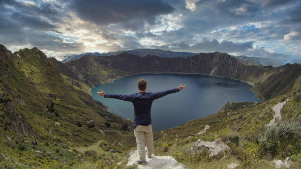 Caucasian backpacker opening his arms and looking at a marvelous lake inside a volcano named Quilotoa. Ecuador, stock photo