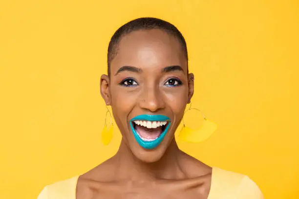Close up portrait of excited young African American woman with fashionable colorful make up isolated on yellow studio background