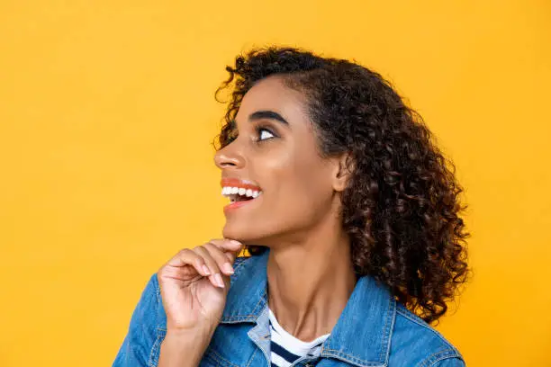 Close up portrait of young smiling African American woman looking at side with hand touching chin on studio yellow studio background