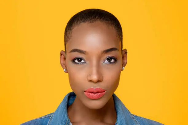 Close up beauty portrait of young African American woman looking at camera in isolated studio yellow background