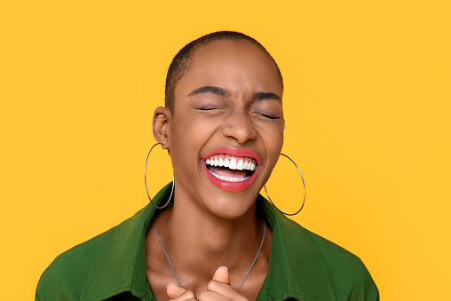 Close up portrait of happy  African American woman laughing with eyes closed in isolated studio yellow background