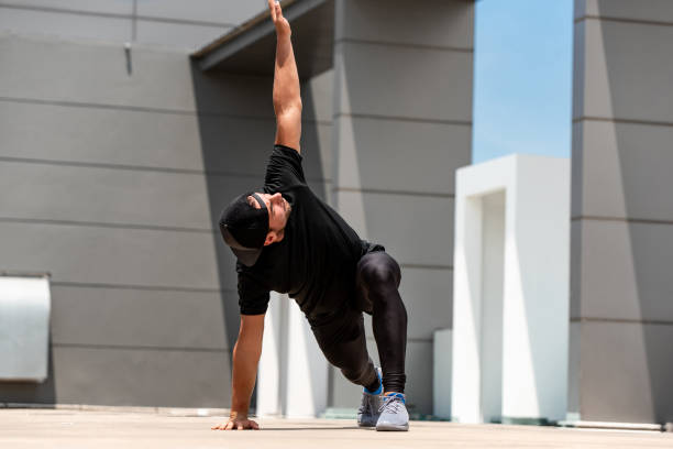 homme de sports d’ajustement réchauffant avec l’exercice de fente d’araignée à l’extérieur sur le plancher de toit de bâtiment - core strength photos et images de collection