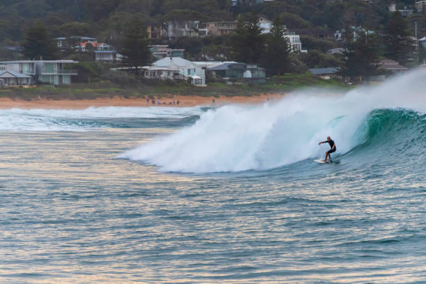 Avoca Beach, NSW, Australia - May 9 2021 : Sunrise surfer catching a wave