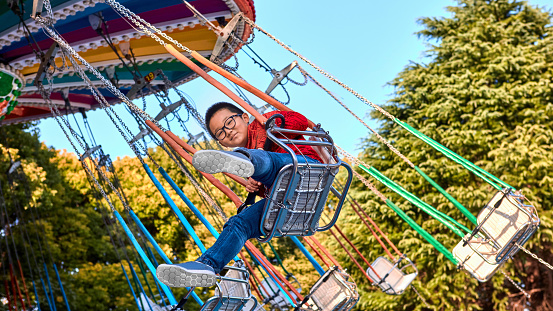 Happy boy riding a spinning chain swing in an amusement park，The Chinese boy rides the revolving chain swing and smiles happily at the camera。Colorful spinning chain swing in the amusement park