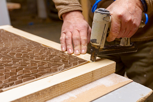 Carpenter puts together planks on the door frame using a pneumatic stapler in the carpentry workshop.