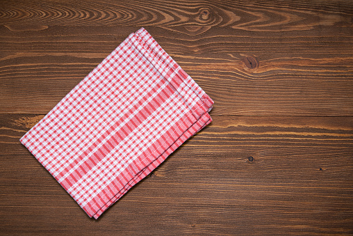 Checkered cloth napkin or kitchen towel on brown wooden surface. Tablecloth on tabletop, top view.