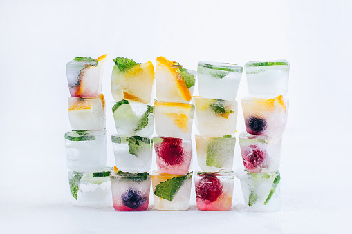 ice cubes with frozen fruits and mint stand pyramid on white background