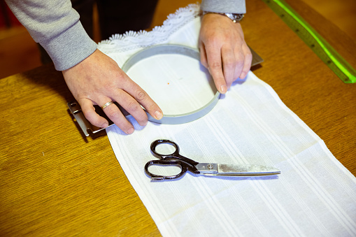 Preparing round metallic embroidery frame on white canvas with sewing scissors, ruler on the table, traditional craft small business
