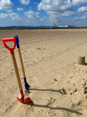 Stock photo showing spades dug into sandy beach beside sandcastles made with a bucket.