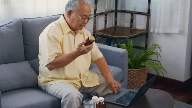 Photo of elderly patient video call by laptop computer to doctor for inquire about which bottle of medication