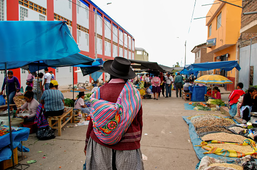 Ayacucho, Peru - January, 2017: Indigenous woman walking on a street market in highlands Peruvian town with traditional ethnic clothes. Quechua female with a hat from behind in a local market.