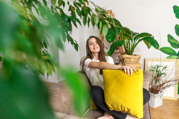 Young smiling woman in couch between plants. Young smiling woman in couch between house plants at home. green home decor stock pictures, royalty-free photos & images
