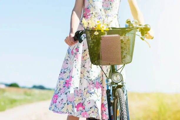 Wild flowers bouquet carried by young woman in dress with flowers in bicycle basket , flowers  gathered in a meadow  by woman in the countryside in summer time sunny day