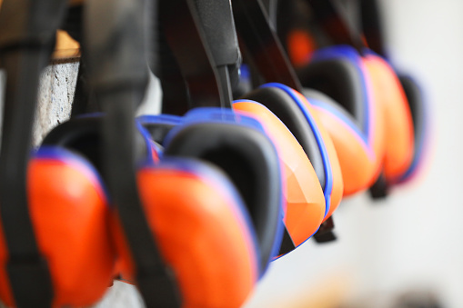 row of orange ear muffs ear protection on a rack. workplace health and safety deafness concept. safe work practice.