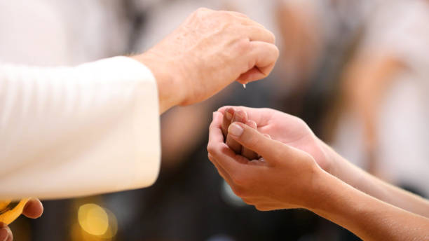 priest at the moment of handing a parishioner the host or bread during mass or holy communion Close up image of a parishoners hands clasped receiving the bread during holy communion from a catholic priest at Mass. liturgy photos stock pictures, royalty-free photos & images