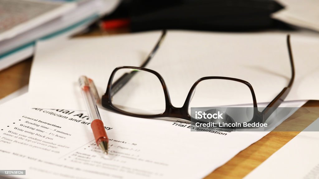 marking exams. Glasses red pen and exam paper a school teachers desk with glasses and exam paper being marked on it. education, educator, teaching concept. Teacher Stock Photo