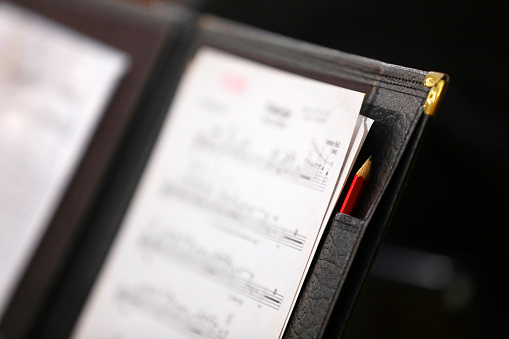 Black leather music score sheet folder with red pencil and brass corner. Close up shallow depth of field. Landscape orientation