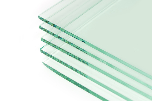Sheets of Factory manufacturing tempered clear float glass panels cut to size. White background.