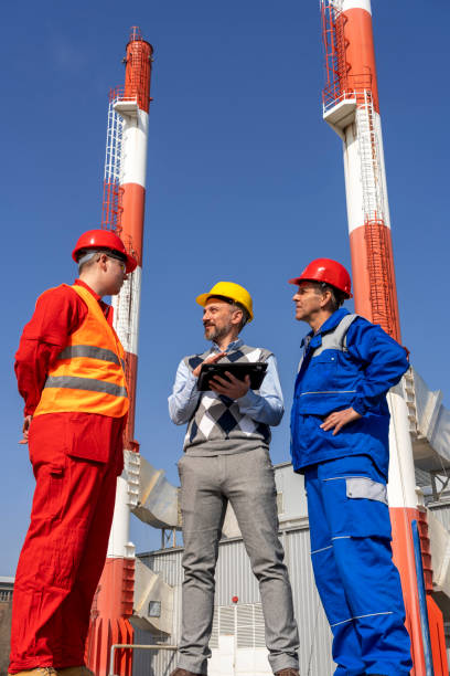istock Manager Using Digital Tablet and Discussing with Two Workers Against Power Plant Chimneys 1317420151