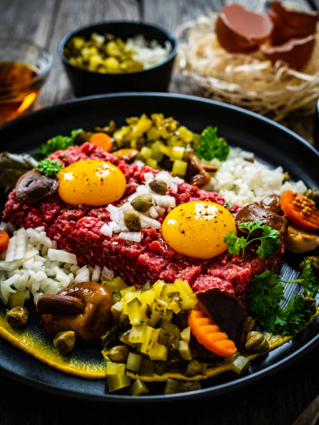 Beef tartare steak with onion, capers and pickled cucumbers on wooden table