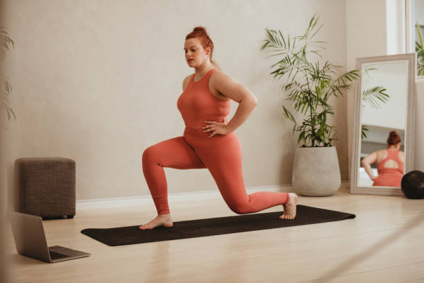 Woman exercising over online workout class Plus size female in sportswear doing lunge workout watching online exercise class. Woman exercising over online workout class on her laptop. lunge stock pictures, royalty-free photos & images
