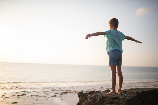 Beautiful young boy raised his hands and breathing fresh air early in the morning, at the beach.