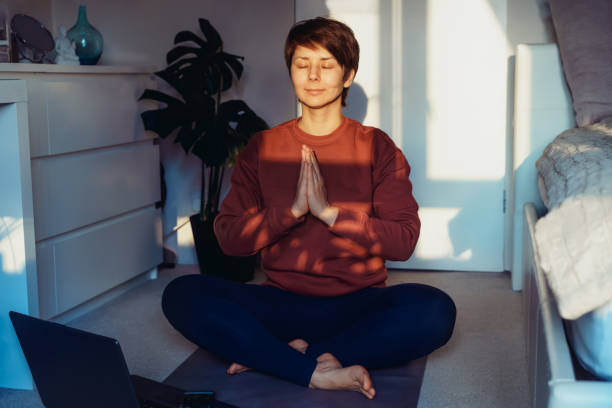 A woman sitting on a mat while doing yoga position Namaste in bedroom. Relaxation online yoga practice at home. Healthy Lifestyle. Home online workout. Fitness online training. Soft selective focus. una mujer sentada en una colchoneta mientras hacía yoga posiciona a namaste en el dormitorio. relajación práctica de yoga en línea en casa. estilo de vida saludable. entrenamiento en línea en casa. entrenamiento en línea de fitness. enfoque selectivo