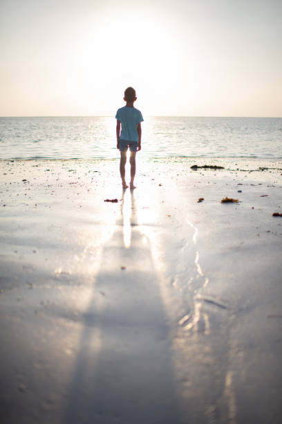 Beautiful young boy looking at the distance, early in the morning, at the beach.