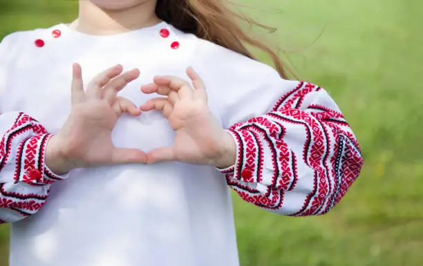 Girl dressed in vyshyvvanka making heart sign with hands. Traditional, ethnic, prints and ornaments. Vyshyvanka.Ukraine. Ukrainian Vyshyvanka`s day.Independence Day of Ukraine.