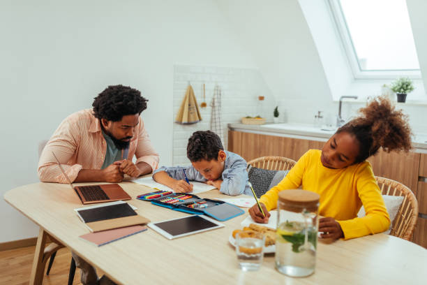 istock Afro students doing homework at home with school books helped by their father. Dad control, help and teaching their children 1317430671