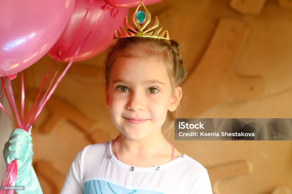 cute little caucasian seven year old children girl at home in a costume elsa  frozen with a golden crown and pink balloons cheerfully celebrates her birthday girl; birthday; kid; frozen; costume; baby; balloons; blue; brown eyes; candid; caucasian; celebrates; cheerful; child; childhood; children; clothes; home; concept; crown; day; domestic; dress; elsa; emotion; fashion; fun; gloves; happiness; happy; holiday; icy heart; indoor; inside; life; lifestyle; light; little; one; party; people; person; pink; portrait; positive; princess; seven year old; smiling; time; toddler Elsa - Frozen Stock Photo