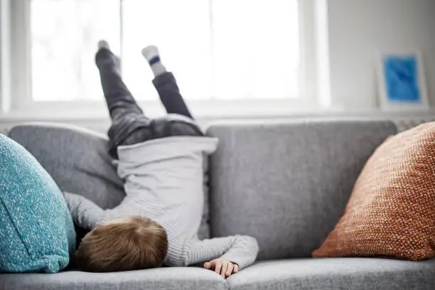 Cute child lying face down on the sofa. Tired boy after leisure activity and cheerful games.