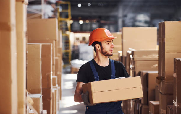 istock Young storage worker in uniform and hard hat carries box in hands 1317435799