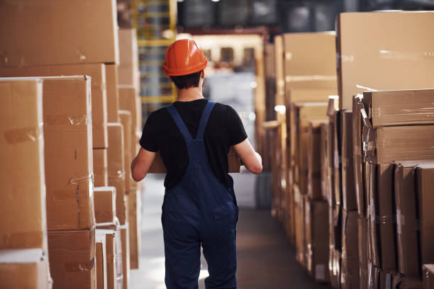 istock Young storage worker in uniform and hard hat carries box in hands 1317435864